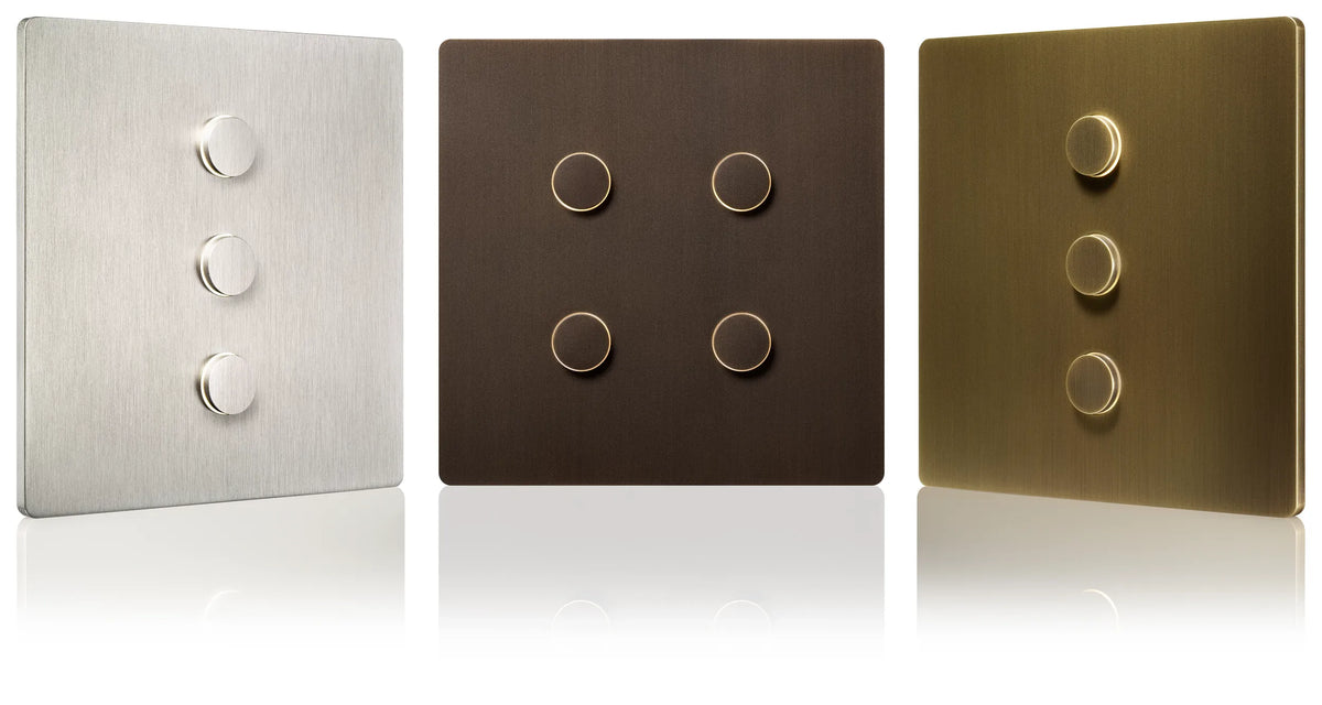Three square Signature metal Lutron Alisse wall plates shown side by side on a white reflective background: Satin Nickle with three round buttons, Aged Bronze with four round buttons, and Aged Brass with three round buttons.