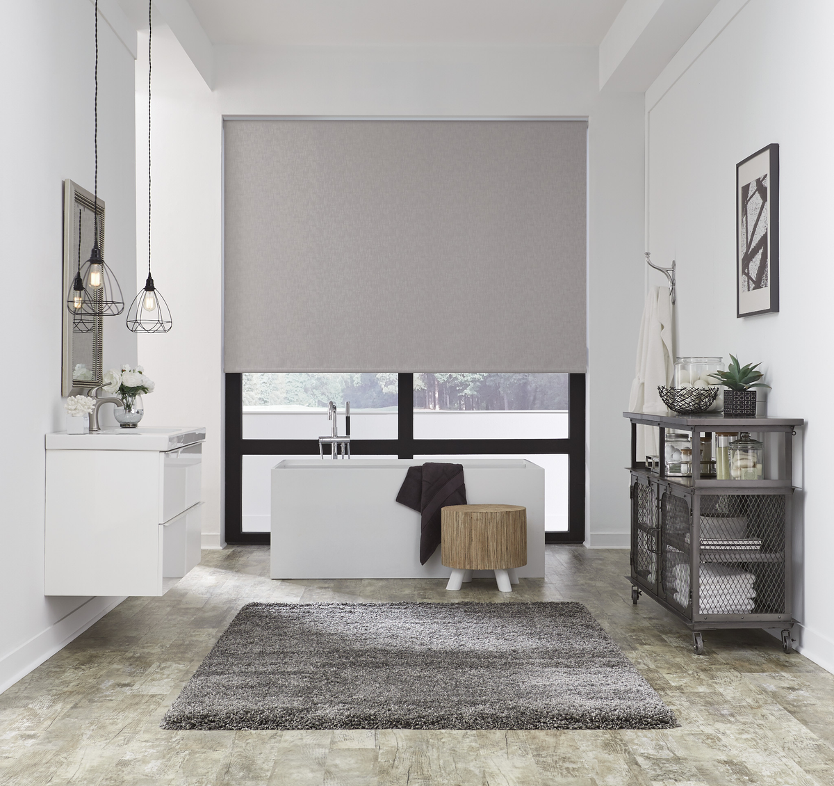 A modern bathroom interior with a gray roller blind mounted above a large black-framed window, next to a white floating vanity and a gray rug on a light stone floor.