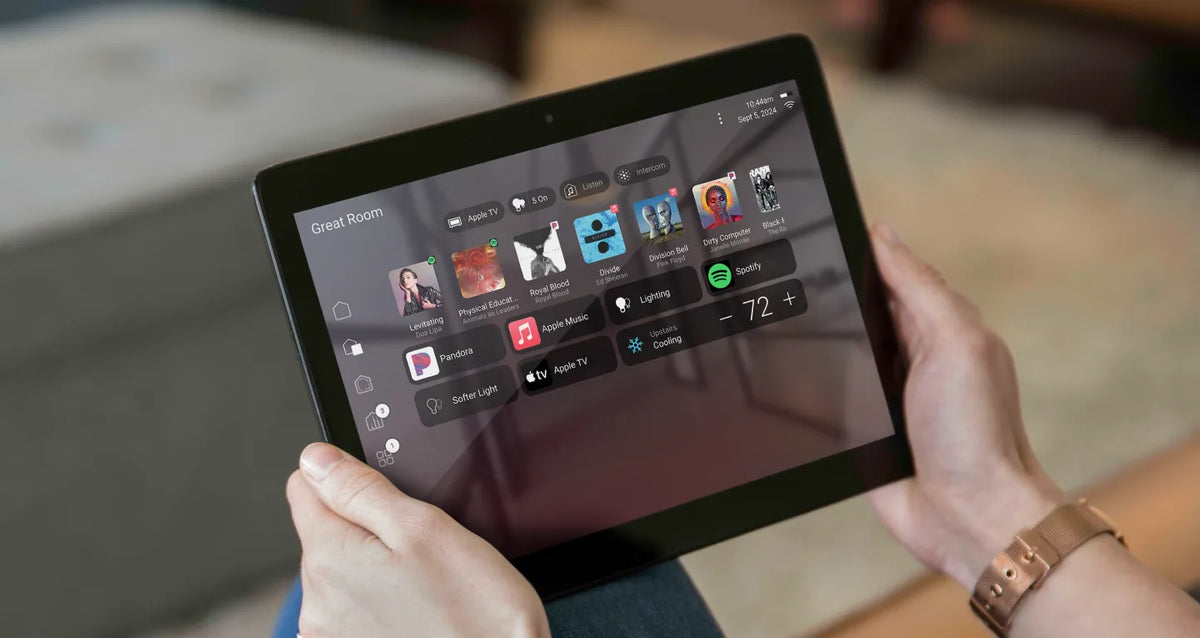 Person holding a tablet with a Control4 home screen on a blurred background.