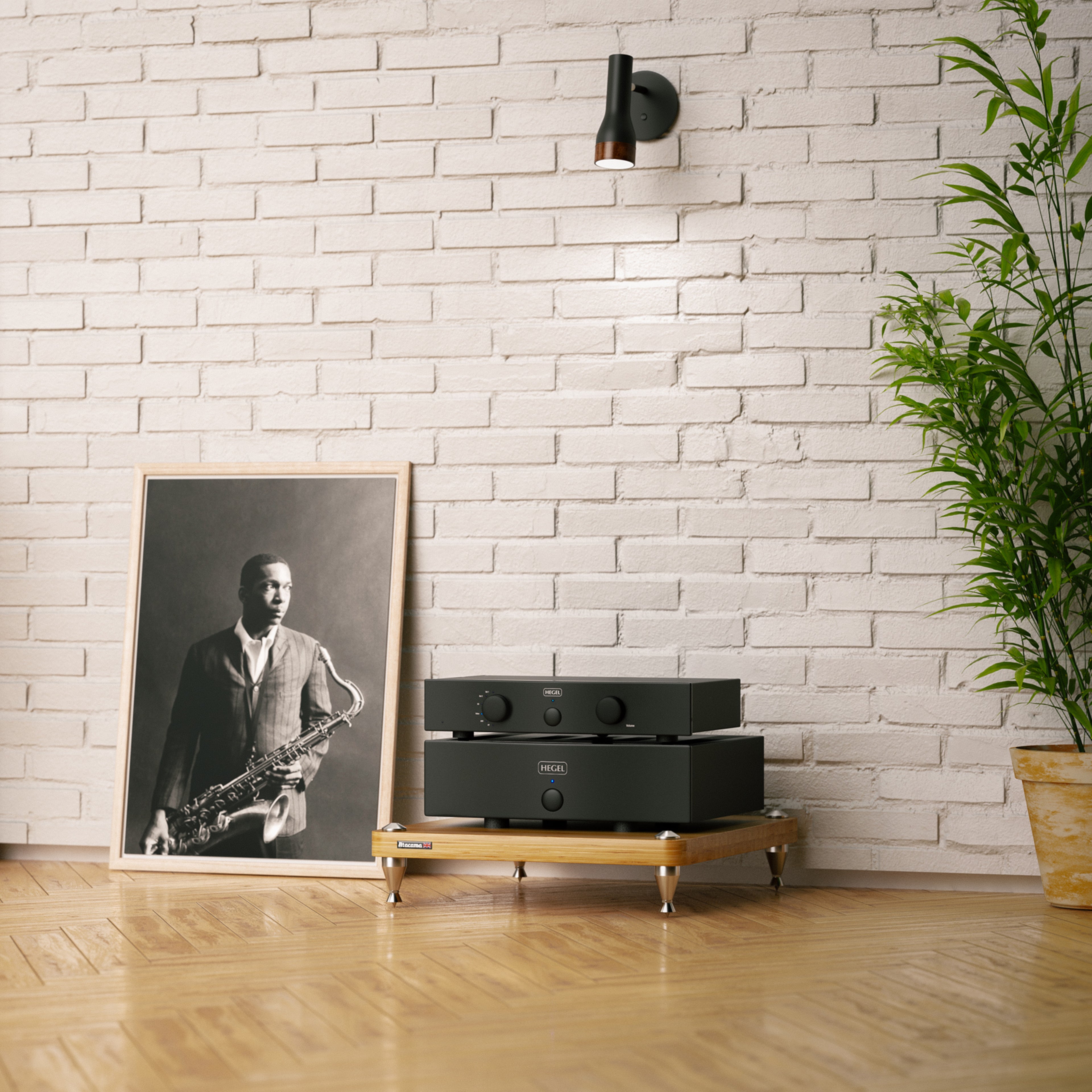 Black Hegel P20 Preamplifier and H20 Amplifier on a wooden stand against a white brick wall with a framed picture and plant.