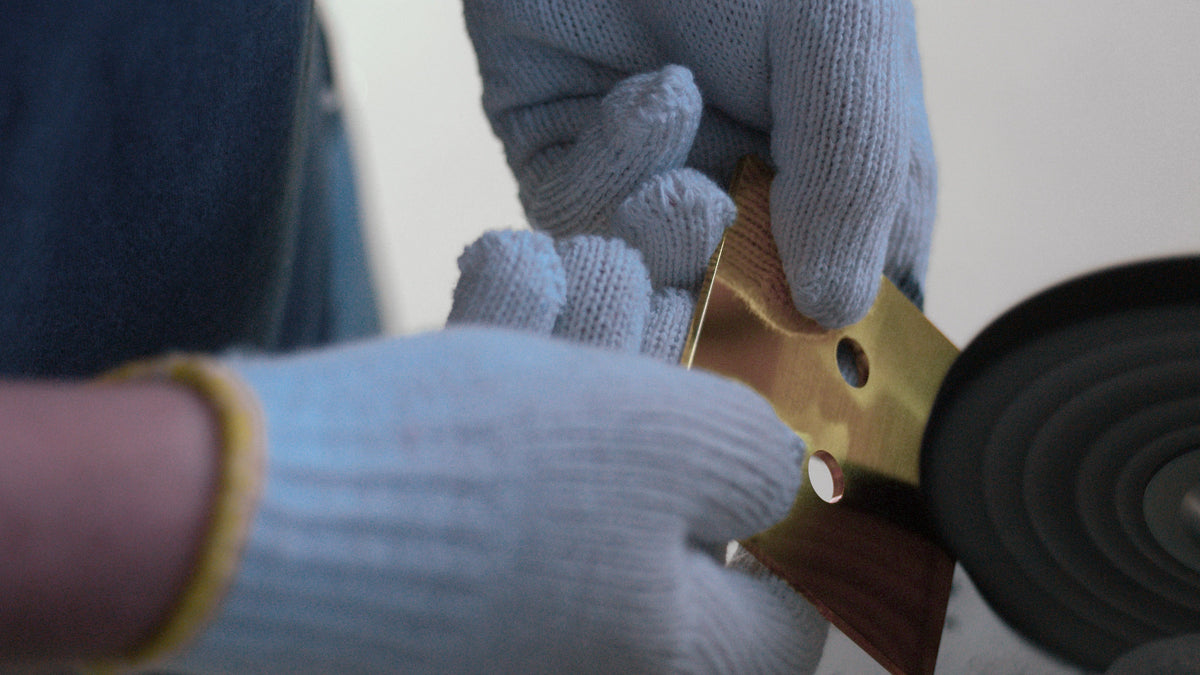 Close-up of a person wearing light blue knit work gloves holding a brass-colored metal component next to a black circular wheel or roller.