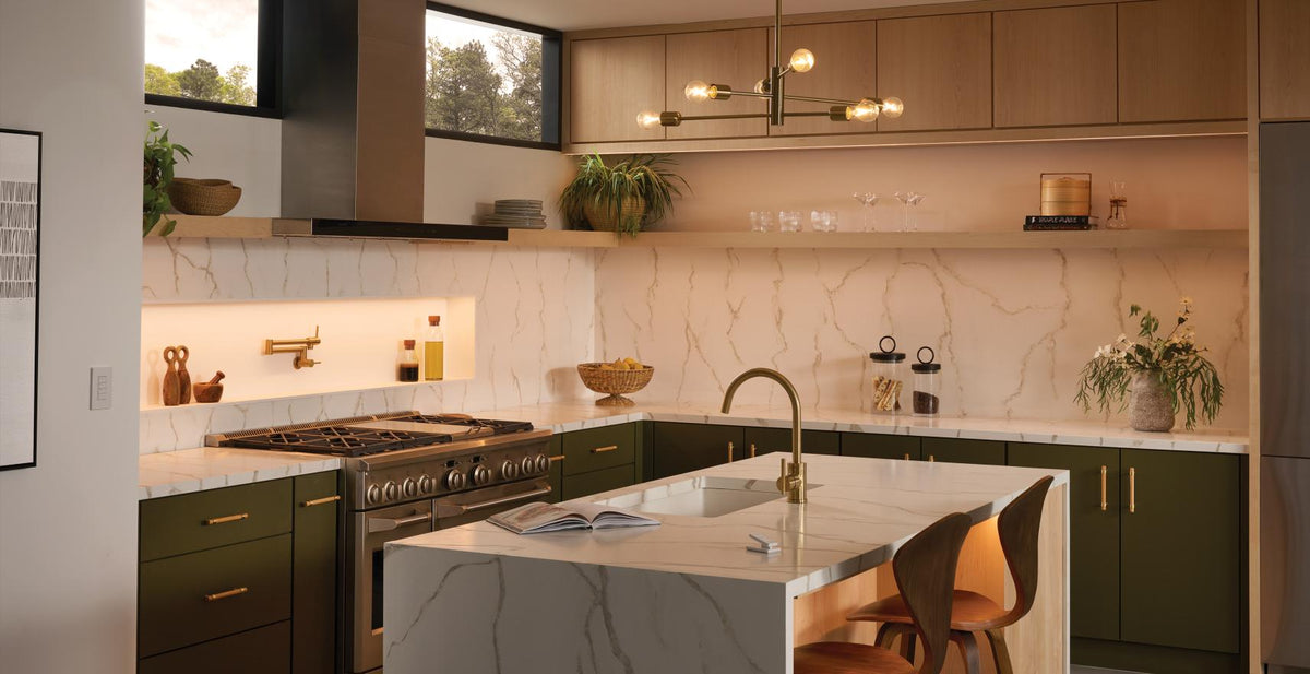 A modern kitchen interior with dark green cabinets, white marble countertops and backsplash, a central island, built-in gas range, pendant lights, and bar stools.