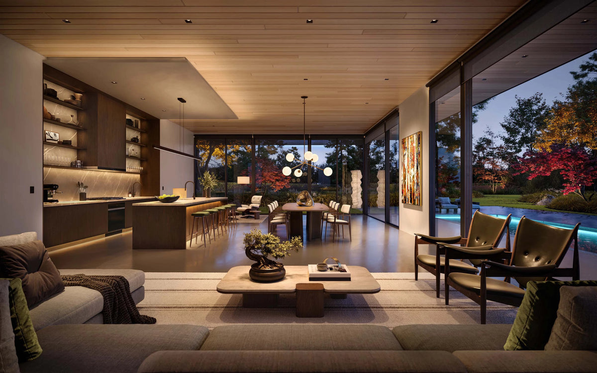 Warm Lutron lighting washes over a modern open-concept living space with a large beige sectional sofa in the foreground, a low rectangular coffee table, two dark wood armchairs, a dining area with a round table and chairs, and a kitchen with wood cabinetry and shelves. Large floor-to-ceiling windows reveal an outdoor evening landscape with trees and a lit pool.