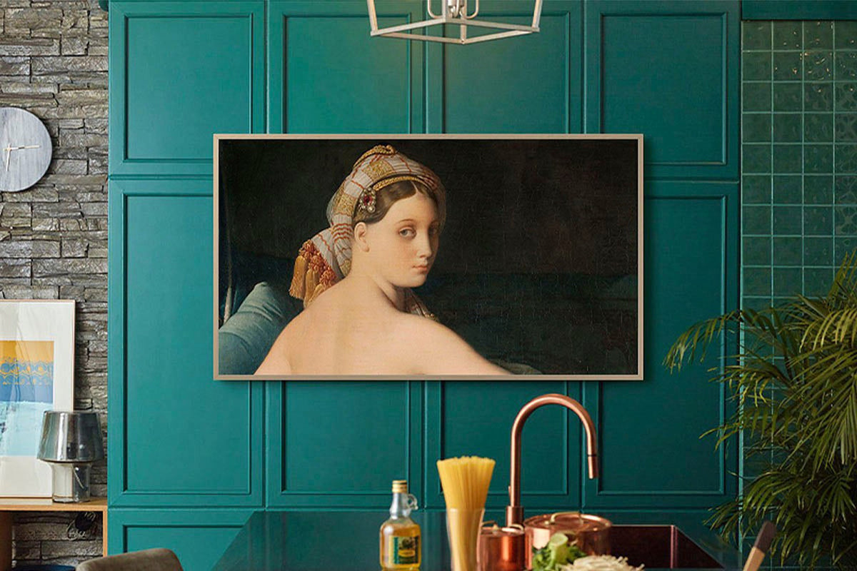 Teal wall with Samsung The Frame TV displaying artwork of a woman's portrait, kitchen counter with bottles and decor.