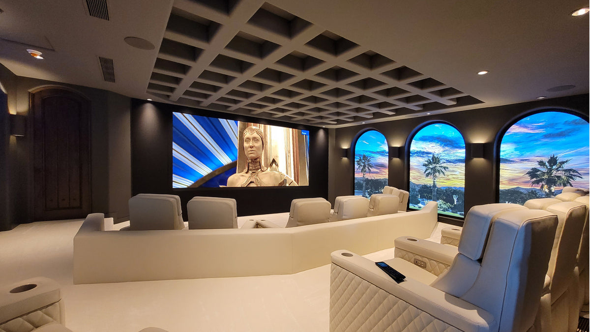 Luxury Wisdom Audio Dolby Atmos home theater with plush cream reclining theater seats, a large curved screen displaying a movie, and three arched window-like panels showing a sunset beach scene.