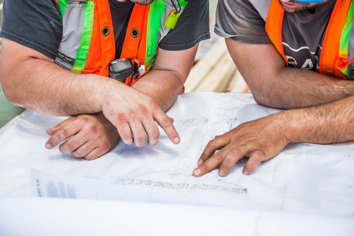Two construction workers in high-visibility vests examining blueprints on a table.